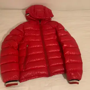 Säljer en snygg röd dunjacka från Moncler i mycket bra skick. Jackan har en dragkedja framtill och långa ärmar med ribbade muddar. Perfekt för vintern med sin varma och puffiga design. Den har också en praktisk huva för extra skydd mot kylan.