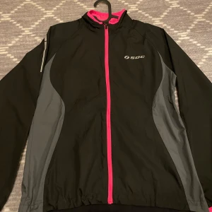 träningsjacka  - Säljer en svart träningsjacka från SOC i mycket bra skick. Jackan har en dragkedja i rosa och gråa detaljer på sidorna. Aldrig använd
