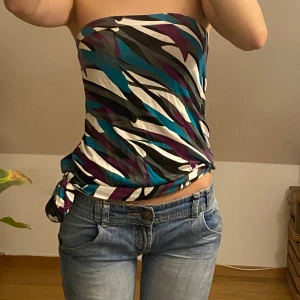 Flerfärgad tubtopp - Säljer en snygg tubtopp med ett coolt mönster. Toppen är köpt med sellpy men aldrig använd och har en knytning på sidan för extra stil. Perfekt för sommaren och fest!