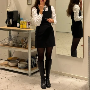 Svart klänning  - Snygg svart klänning med en vit långärmad skjorta under (sälja separat). Perfekt för en stilren och klassisk look. Klänningen har en dragkedja bak och är i ett normal passform. Passar bra till både vardag och festliga tillfällen.