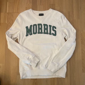 Sweatshirt Morris  - Vit sweatshirt med grönt tryck framtill. Från Morris. Tröjan har en rund halsringning och långa ärmar. Storlek M. Har en liten diskret fläck (se bild 3) 
