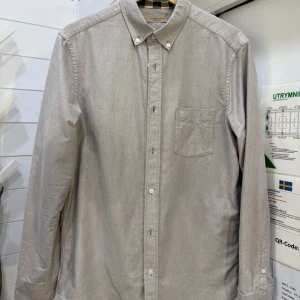 Grå skjorta från Burberry Brit - Säljer en stilren grå skjorta från Burberry Brit i mycket bra skick. Skjortan är långärmad och har klassiska knappar framtill. Den är gjord av bomull och har Burberrys ikoniska rutiga mönster på insidan av kragen och ärmsluten. Perfekt för både vardag och fest!