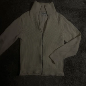 Beige ribbad tröja från Carhartt - Säljer en snygg beige ribbad tröja från East West. Den har en dragkedja framtill och långa ärmar, perfekt för kyliga dagar. Tröjan är i bra skick och passar både till vardags och lite finare tillfällen. Skön och stilren design!
