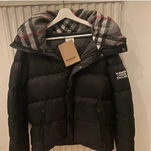Burberry jacka - Säljer en snygg svart pufferjacka från Burberry blir till jacka och väst med klassiskt rutigt foder. Jackan har en dragkedja och knappar för extra skydd mot kylan. Perfekt för höst och vinter, håller dig varm och stilren. Passar både till vardags och festliga tillfällen. 🖤