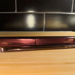 Hourglass vinklad sminkborste - Säljer en snygg vinklad sminkborste från Hourglass, perfekt för precisionsarbete som eyeliner eller ögonbryn. Den har en elegant design med ett mörkrött handtag och mjuka borst. Perfekt för att skapa skarpa linjer och detaljer i din sminkrutin. Nypris 435 kr