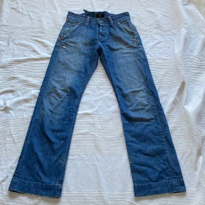 Blå jeans från Lee - Säljer ett par snygga blå jeans i så fin sliten tvätt från Lee! Välanvända men i bra skick förutom att en knapp i gylfen saknas (dock inget jag tkr märks när de är stängda) och att de är slitna längst ner vid hälarna. Midja ca. 39cm men går att justera både mindre och lite större med spännet där bak. 