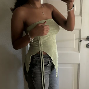 Ljusgrön tubtopp med knytning - Säljer en superfin ljusgrön tubtopp. Den är axelbandslös och har en snygg knytning framtill som du kan knyta som du vill vilket ger en cool detalj. Perfekt för sommaren och festliga tillfällen! Toppen är tight och sitter bra på kroppen.