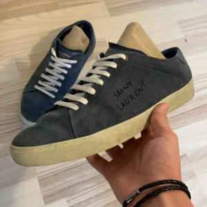 SL/06 sneakers  - Tja! Säljer ett par as feta Yves Saint Laurent i modellen SL/06. Skorna har tagits hand om väll men det finns en defekt på högra skon på mockan vid hälen!(kan skicka bild). Nypris ca 7000kr mitt pris 3800kr. Obs inget OG. Skriv om ni har några frågor