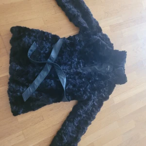 Svart pälsjacka med bälte - Säljer en supermysig svart pälsjacka med bälte. Jackan är långärmad och perfekt för kalla dagar. Den har en elegant och lyxig känsla, och bältet i midjan ger en snygg passform. Perfekt för både vardag och fest!