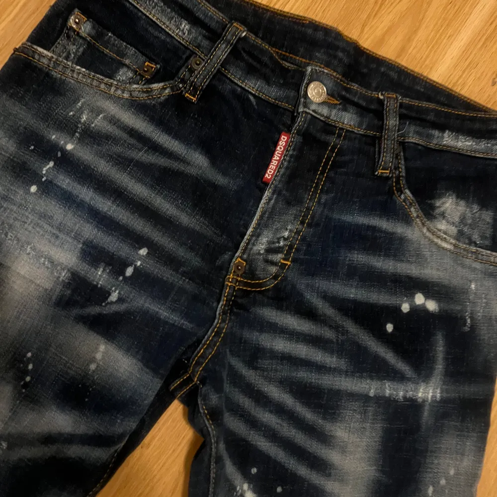 Säljer ett par snygga mörkblå jeans från Dsquared2 i storlek 42. De har en cool distressed look med slitningar och färgstänk. Perfekta för en casual och trendig stil. Jeansen har en dragkedja och knappar framtill. jeansen är äkta ! endast seriösa köpare .. Jeans & Byxor.