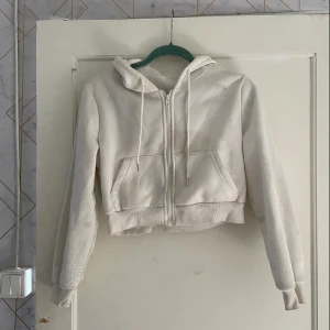 Vit croppad hoodie från Shein - Säljer en vit croppad hoodie från Shein i storlek M. Den är gjord av 100% polyester och har en dragkedja framtill samt en huva med snören. Perfekt för en avslappnad och bekväm stil. Den är i välanvänt skick men fortfarande mysig och funktionell.