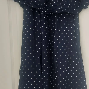 Mörkblå prickig klänning - Säljer en superfin mörkblå klänning med vita prickar. Klänningen är perfekt för sommarens alla fester och har en söt offshoulder-design. Den är i nyskick och passar perfekt för en dag på stan eller en kväll ute. Materialet känns lätt och luftigt, vilket gör den bekväm att bära hela dagen.