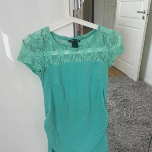 Turkos blommig t-shirt - Fin turkos T-shirt med blommiga detaljer på lite av tröjan. Oanvänd och säljer då den är lite stor.