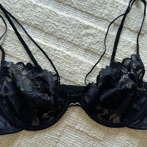 Svart spets-bh med hjärtformade detaljer - Säljer en superfin svart spets-bh med hjärtformade detaljer🤍. Den har tunna axelband och en söt liten hjärtformad detalj i mitten. Det går smala band över brösten som ramar in och framhäver brösten på ett väldigt fint sätt🌸. Perfekt för en romantisk kväll eller bara för att känna sig extra fin😉. Bh:n är oanvänd och är i storlek 80D.