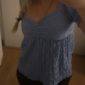 Blå topp med öppen rygg - Säljer en söt blå topp med korta ärmar och öppen rygg. Toppen har en rynkad detalj framtill och är gjord av ett lätt och luftigt material. Perfekt för sommardagar eller en avslappnad festkväll. 💙