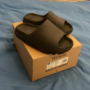 Svarta Adidas Yeezy Slide ”onyx” - Säljer ett par svarta Adidas Yeezy Slide ”onyx”. Dessa sandaler har en stilren design med en bred rem över foten. Storlek 39 skick 8/10 man kan se på undersidan att dem är använda en några fåtal gånger. Jag köpte dem för något år sen men dem var för små och sedan dess har dem bara legat och skräpt i garderoben. Dem är köpta på adidas confirmed appen. Pris kan diskuteras, skriv om du har någon fråga.