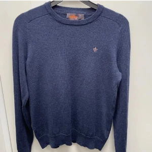 Morris merinoull tröja - Snygg blå merinoulls tröja med rund hals och ett litet broderat emblem på bröstet. Tröjan har ribbade kanter vid ärmslut och nederkant. Perfekt för en stilren look. Hör av dig vid frågor och funderingar. Mvh Emil