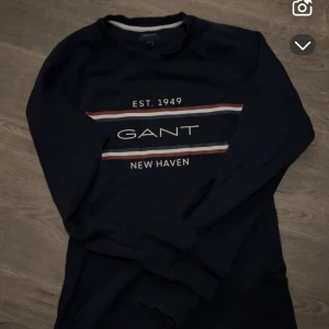 Svart långärmad tröja från GANT - Säljer en stilren svart långärmad tröja från GANT med tryck 'EST. 1949 NEW HAVEN' i vitt och rött.