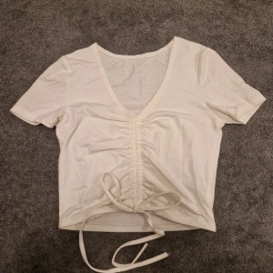 Vit v-ringad topp med knyt - Säljer en stilren vit topp med v-ringning och knytning framtill. Toppen har korta ärmar och är perfekt för en avslappnad look.