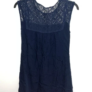Mörkblå klänning med spetsdetaljer - Snygg mörkblå klänning med spetsdetaljer upptill och ett knytband i midjan. Perfekt för en fin look. Klänningen är ärmlös och har en normal passform.