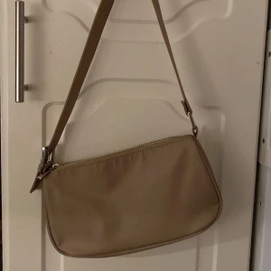 Beige axelväska med dragkedja - Snygg beige axelväska med justerbar rem och dragkedja. Perfekt för att bära dina nödvändigheter med stil. Enkel och stilren design som passar till många outfits.