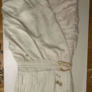 Vit klänning med plisserad kjol - Elegant vit klänning med plisserad kjol och markerad midja. Perfekt för sommarens festligheter. Den har en vacker struktur och en klassisk look som passar många tillfällen.