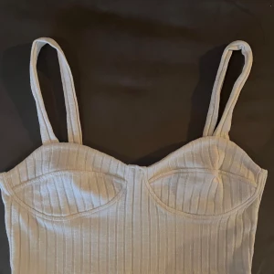 Vit ribbad linnetopp från Monki - Säljer en stilren vit ribbad linnetopp från Monki. Toppen har smala axelband och en enkel design som passar perfekt till sommaren. Perfekt för en avslappnad look eller att styla upp med accessoarer.