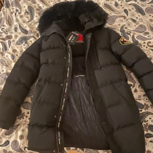 Zavetti canada vinterjacka (Storlek S) - Säljer en svart dunjacka från Zavetti Canada med pälsdetalj på huvan. Jackan har en långärmad design och dragkedja framtill. Perfekt för kalla vinterdagar. 🖤Jackan är helt oanvänd. Nypris (1500)