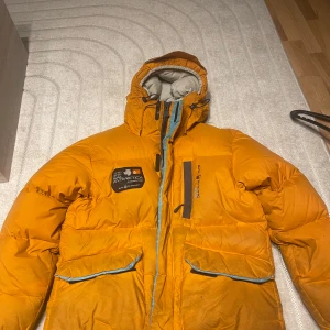 Orange dunjacka från Sail Racing - Säljer en cool orange dunjacka från Sail Racing. Jackan har en hög krage och justerbar huva, perfekt för kalla dagar. Den har dragkedja och flera praktiska fickor med blå detaljer. Insidan är ljusgrå och ger en snygg kontrast. Perfekt för vintern! 🧡ops priset kan diskuteras först till kvarn!! Inget sönder med den