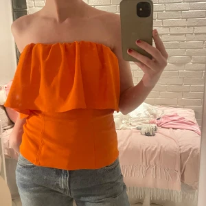 Orange axelbandslös topp - Säljer en snygg orange axelbandslös topp med volangdetalj. Så fin till sommaren när man är brun🧡🧡🧡🧡aldrig använd endast testad🥰🥰