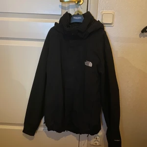 Svart jacka från The North Face - Säljer en stilren svart jacka från The North Face. Jackan har en normal passform med långa ärmar och en praktisk huva. Perfekt för kyligare dagar med sitt slitstarka material och diskreta logga på bröstet. Ett måste för garderoben! 🖤