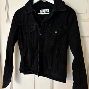Svart jeansjacka från Stay - Snygg svart jeansjacka från Stay med klassisk design. Jackan har knappar framtill och två bröstfickor med lock. Perfekt för en stilren look.