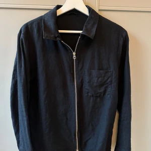 Svart jacka från J.Lindeberg - Snygg svart jacka från J.Lindeberg med dragkedja framtill och en bröstficka. Jackan har en klassisk krage och är långärmad. 