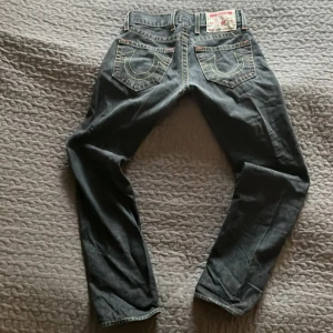 Jeans från True Religion - Snygga jeans från True Religion med klassisk femficksdesign och kontrastsömmar. De har en mörk tvätt och tydliga sömmar på bakfickorna. Perfekta för en avslappnad stil. Row 28 och seat 33. Modellen är Logan! Hör av er vid frågor eller prisförslag.