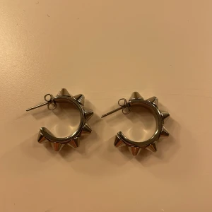 Silvriga örhängen med nitar från Edblad - Snygga silvriga örhängen från Edblad med coola nitar runt hela ringen. Perfekta för att ge en edgy touch till din stil. Lätta att bära och passar till många olika outfits. 