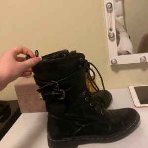 Svarta boots med snörning och dragkedja - Snygga svarta boots med både snörning och dragkedja för enkel på- och avtagning. De har en robust design med spänne upptill för extra stil och funktionalitet.