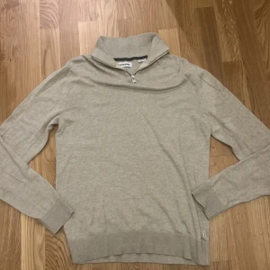 Beige tröja med dragkedja från Jack & Jones - Säljer en stilren beige tröja från Jack & Jones med dragkedja vid halsen. Tröjan har långa ärmar och ribbade muddar vid ärmslut och nederkant. Perfekt för en avslappnad stil.