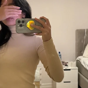 Beige polotröja - Säljer en stilren beige polotröja med långa ärmar. Tröjan är croppad och passar perfekt för en trendig look. Perfekt för kyligare dagar och kan enkelt matchas med olika outfits.