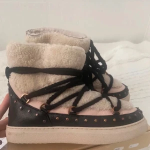 Inuikki  - Säljer ett par unika boots med beige och svart design. De har en varm fodring och dekorativa nitar runt sulan. Skorna har snörning som ger en cool look.