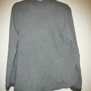 Grå hoodie - Säljer en enkel och bekväm grå hoodie med långa ärmar och hood. Perfekt för en avslappnad stil. Den har ribbade muddar vid ärmslut och nederkant. Hooden fodrad med ett svart mönstrat bomullstyg. 