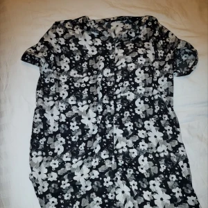 Svart och vit blommig oversized skjorta - Säljer en svart och vit blommig skjorta med korta ärmar. Perfekt för en somrig look med sitt fina blommönster. Klänningen har en avslappnad passform och är gjord i ett lätt material.