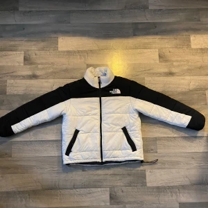 Svart och vit dunjacka från The North Face - Säljer en snygg svart och vit dunjacka från The North Face. Jackan har en dragkedja framtill och två praktiska fickor. Några små hål på framsidan men annars sparsamt använd.