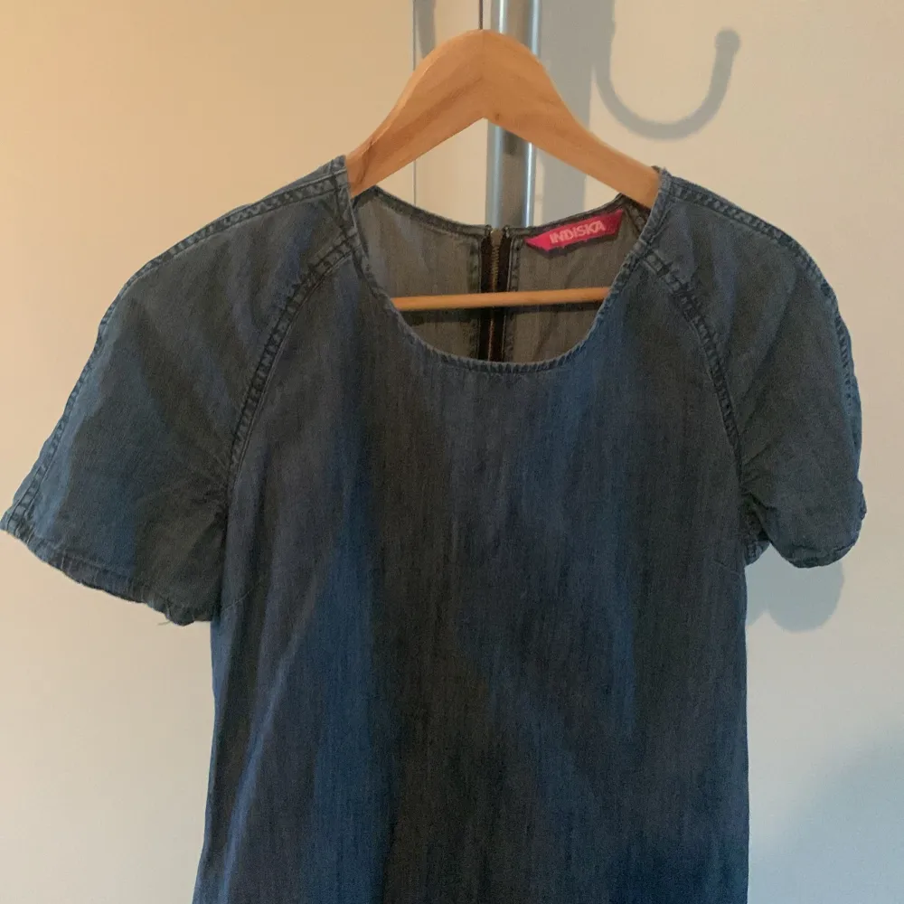 Säljer en stilren blå jeansklänning från Indiska. Klänningen har korta ärmar och en rund halsringning. Perfekt för en avslappnad look. Den är gjord i ett mjukt denimtyg som ger en skön känsla.. Mekot.