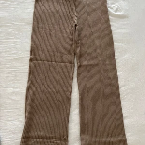 Beige ribbade byxor - Säljer ett par snygga beige ribbade byxor med en loose passform. Perfekta för en avslappnad stil och kan enkelt matchas med olika toppar. Byxorna har en hög midja och är tillverkade i ett mjukt material som ger en bekväm känsla.