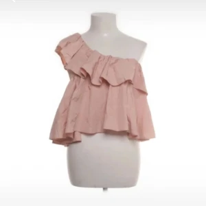 Rosa oneshoulder topp med volang - Säljer en söt rosa oneshoulder topp med volangdetaljer. Perfekt för sommarens varma dagar. Toppen har en luftig passform och är tillverkad i ett lätt material.