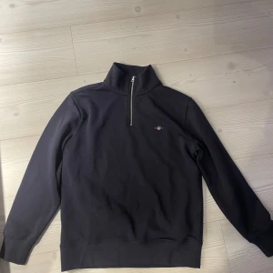 Svart tröja med dragkedja från GANT - Säljer en svart tröja från GANT med halv dragkedja och broderad logo på bröstet, aldrig använd! Ny pris 1500! Pris går att diskutera😊