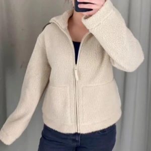 Beige teddyjacka - Säljer denna populära och mysiga teddyjackan med dragkedja framtill. Jackan har en hög krage och långa ärmar, perfekt nu till våren! Den är i väldigt bra skick och endast använd ett fåtal gånger.