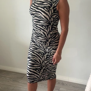 Zebramönstrad klänning - Snygg zebramönstrad klänning med ärmlös design och tight passform. Perfekt för att sticka ut med sitt djärva mönster. Klänningen har en klassisk svart och vit färgkombination som ger en tidlös look.