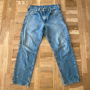 Blå jeansbyxor Carhartt - Säljer ett par klassiska blå carhartt jeansbyxor med en straight passform. Byxorna har en midwaist design och relaxed fit. De har en sliten look med en del målarfärgs fläckar utspritt. 