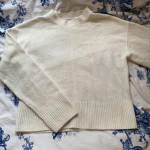 Vit stickad tröja - Säljer en stilren vit stickad tröja med ribbade detaljer vid ärmslut och nederkant. Perfekt för kyligare dagar och enkel att matcha med olika outfits. Tröjan har långa ärmar och en klassisk rund halsringning.